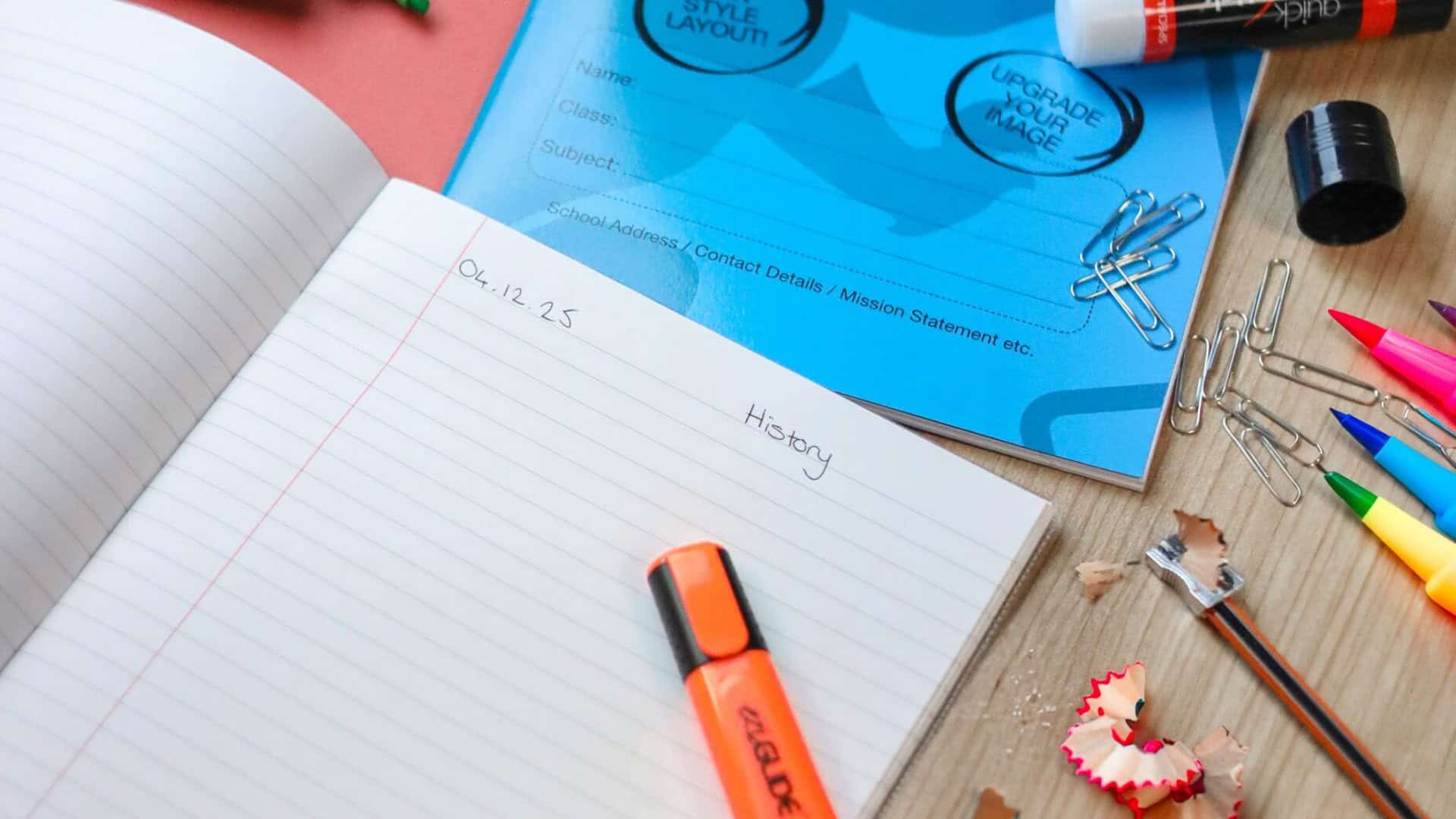 Stack of colourful exercise books placed neatly on a classroom desk, showcasing different sizes and styles.